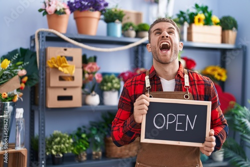 Young caucasian man working at florist holding open sign angry and mad screaming frustrated and furious, shouting with anger looking up.