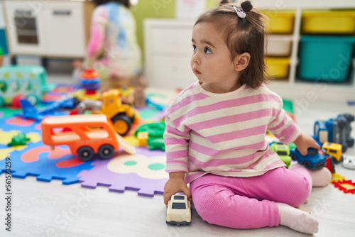 Adorable chinese toddler playing with cars toys sitting on floor at kindergarten