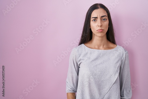 Young brunette woman standing over pink background depressed and worry for distress, crying angry and afraid. sad expression.