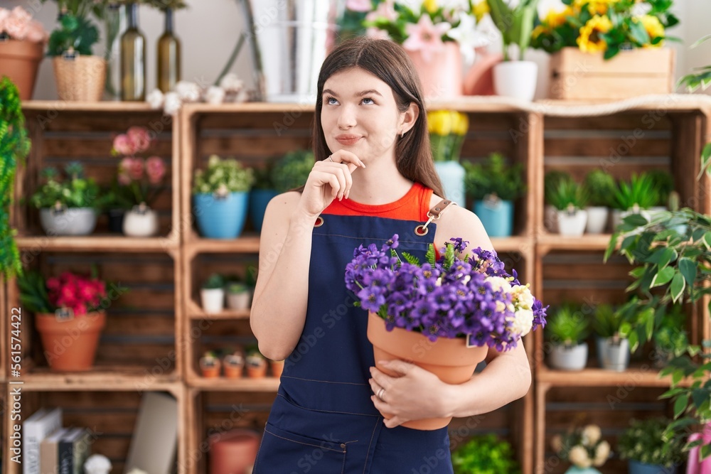 Young caucasian woman working at florist shop holding pot with flowers serious face thinking about question with hand on chin, thoughtful about confusing idea Young caucasian woman working at florist shop holding pot with flowers serious face thinking about question with hand on chin, thoughtful about confusing idea