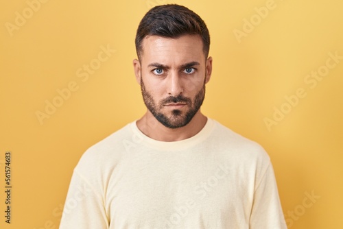 Handsome hispanic man standing over yellow background relaxed with serious expression on face. simple and natural looking at the camera.