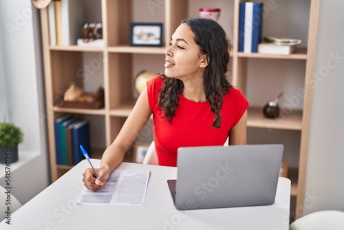 Young african american woman using laptop writing on document sitting on table at home