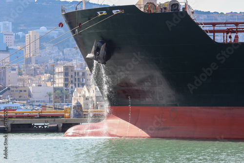 Fotografie, Obraz Large anchored cargo ship discharging ballast water out from Anchor's hub