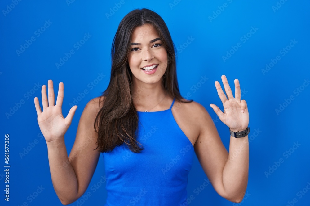 Hispanic woman standing over blue background showing and pointing up with fingers number nine while smiling confident and happy. Hispanic woman standing over blue background showing and pointing up with fingers number nine while smiling confident and happy.