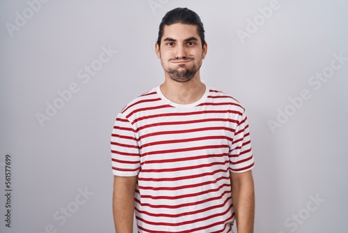 Hispanic man with long hair standing over isolated background puffing cheeks with funny face. mouth inflated with air, crazy expression. photo