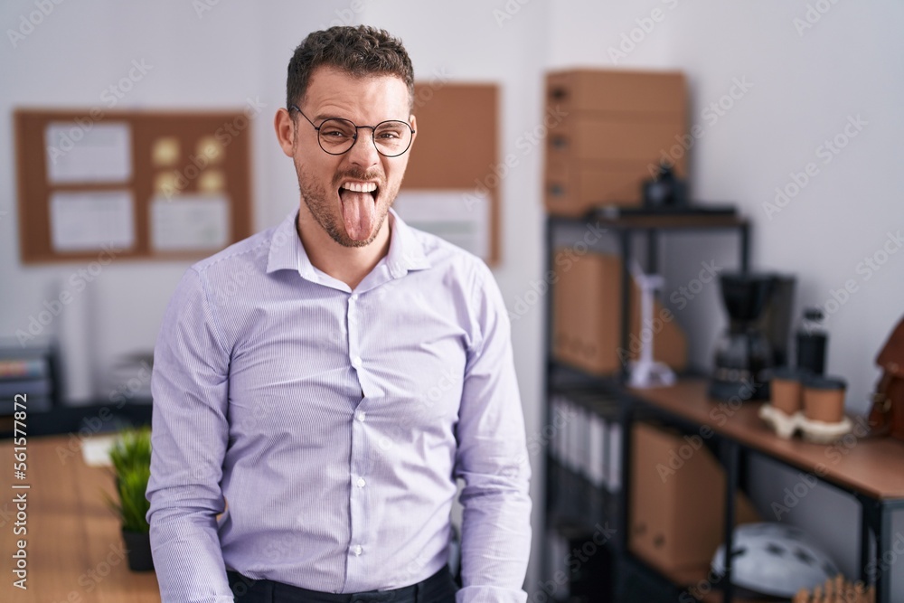 Young hispanic man at the office sticking tongue out happy with funny expression. emotion concept. Young hispanic man at the office sticking tongue out happy with funny expression. emotion concept.