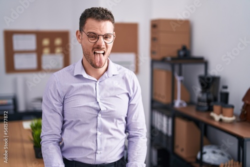 Young hispanic man at the office sticking tongue out happy with funny expression. emotion concept.