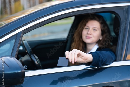 Beautiful happy cheerful girl, young positive woman is paying with credit plastic card from her car smiling, holding out bank card from opened automobile window. Payment for purchases, fast food auto