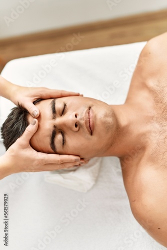 Young hispanic man relaxed having facial massage at beauty center