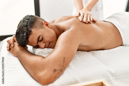 Young hispanic man relaxed having back massage at beauty center