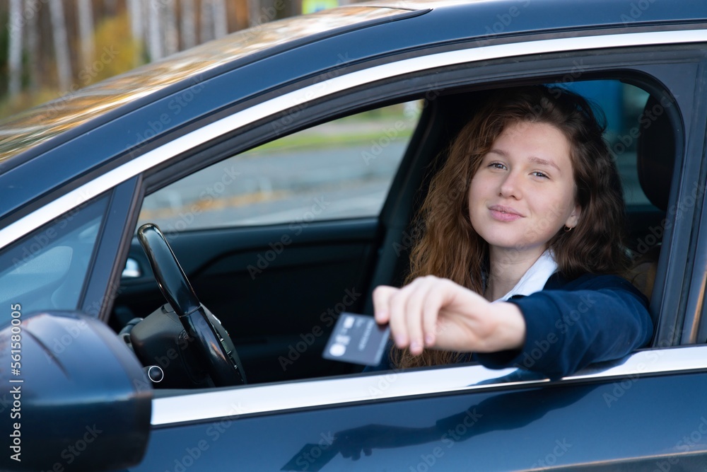 Beautiful happy cheerful girl, young positive woman is paying with credit plastic card from her car smiling, holding out bank card from opened automobile window. Payment for purchases, fast food auto Beautiful happy cheerful girl, young positive woman is paying with credit plastic card from her car smiling, holding out bank card from opened automobile window. Payment for purchases, fast food auto