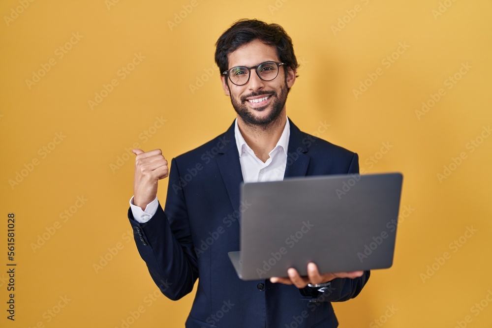 Handsome latin man working using computer laptop pointing to the back behind with hand and thumbs up, smiling confident Handsome latin man working using computer laptop pointing to the back behind with hand and thumbs up, smiling confident