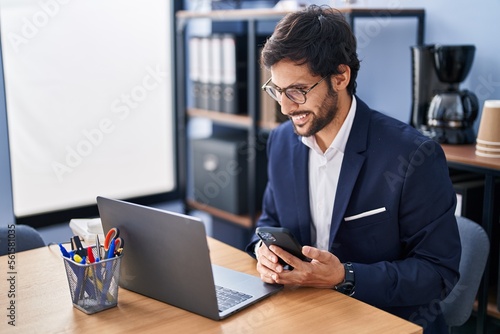 Young hispanic man business worker using laptop and smartphone at office