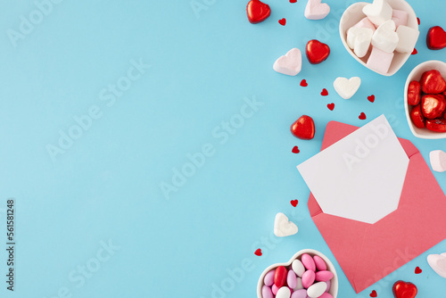Valentines Day celebration concept. Top view photo of envelope with letter, heart shaped saucers with candies and marshmallow on blue background with copy space.