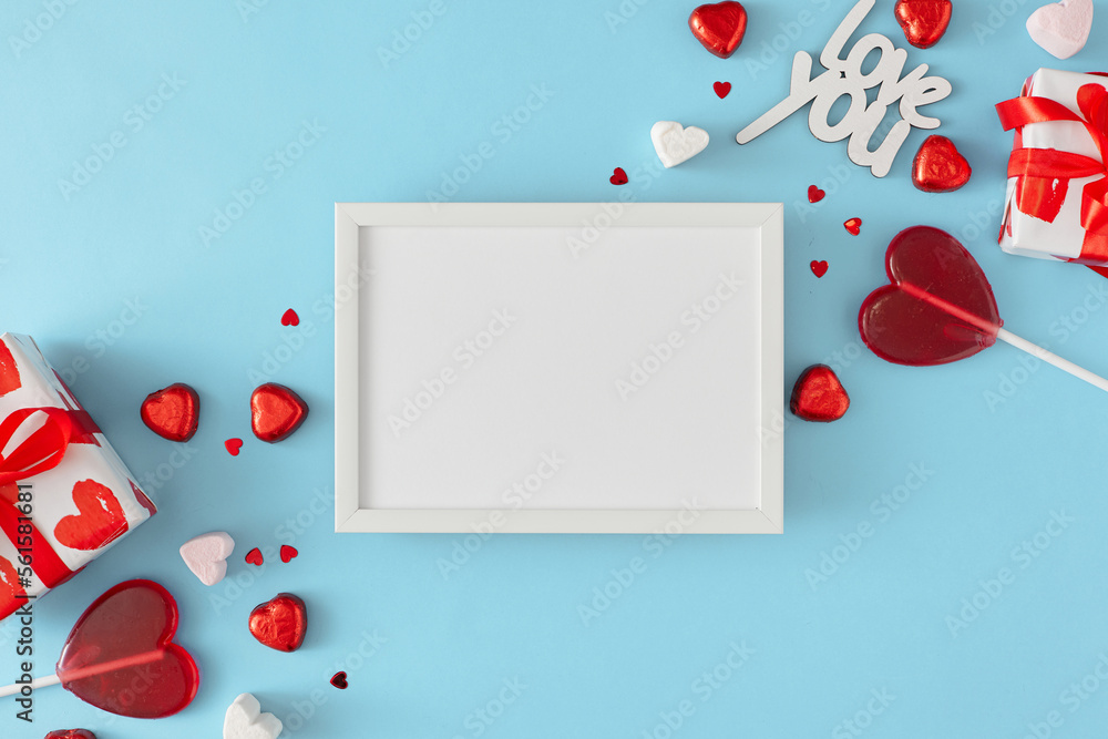 Valentines sweet concept. Flat lay photo of heart shaped chocolate candies, red lollipops, gift boxes, inscription love you on pastel blue background with frame in the middle. Women's day card idea. Valentines sweet concept. Flat lay photo of heart shaped chocolate candies, red lollipops, gift boxes, inscription love you on pastel blue background with frame in the middle. Women's day card idea.