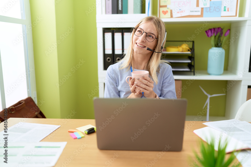 Young blonde woman call center agent using laptop drinking coffee at office Young blonde woman call center agent using laptop drinking coffee at office
