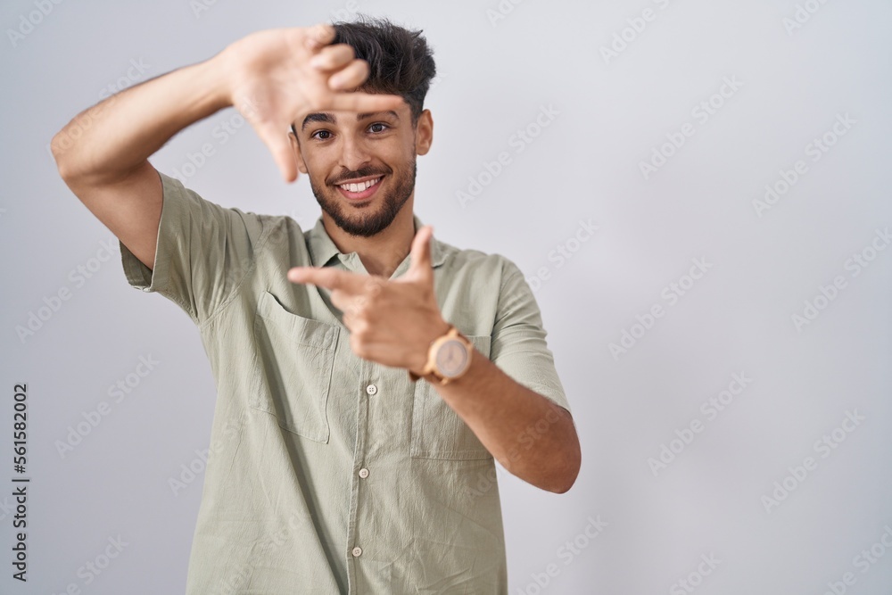 Arab man with beard standing over white background smiling making frame with hands and fingers with happy face. creativity and photography concept. Arab man with beard standing over white background smiling making frame with hands and fingers with happy face. creativity and photography concept.