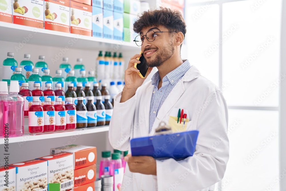 Young arab man pharmacist talking on smartphone reading document at pharmacy Young arab man pharmacist talking on smartphone reading document at pharmacy