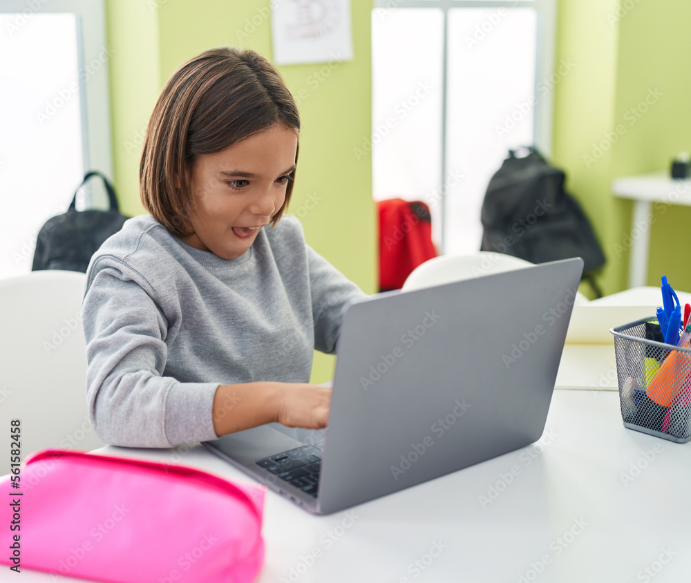 Adorable hispanic boy student using laptop sitting on table at classroom Adorable hispanic boy student using laptop sitting on table at classroom