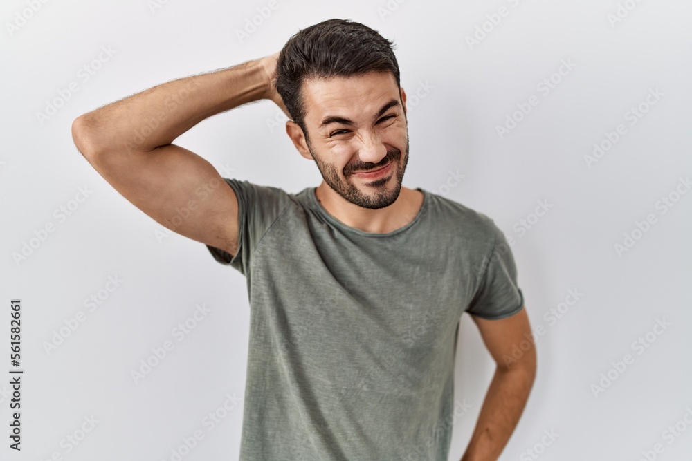 Young hispanic man with beard wearing casual t shirt over white background confuse and wonder about question. uncertain with doubt, thinking with hand on head. pensive concept. Young hispanic man with beard wearing casual t shirt over white background confuse and wonder about question. uncertain with doubt, thinking with hand on head. pensive concept.