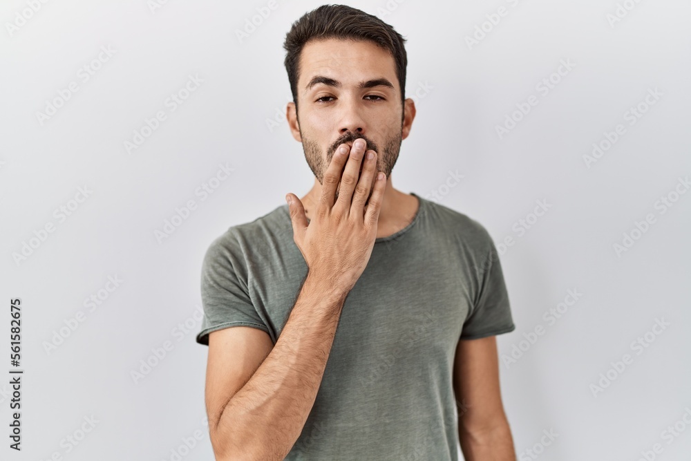 Young hispanic man with beard wearing casual t shirt over white background bored yawning tired covering mouth with hand. restless and sleepiness. Young hispanic man with beard wearing casual t shirt over white background bored yawning tired covering mouth with hand. restless and sleepiness.