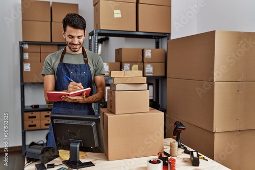 Photos Young hispanic man business worker writing on notebook at storehouse