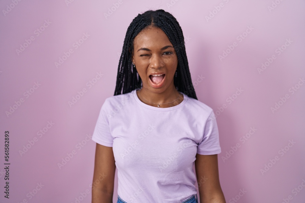 African american woman with braids standing over pink background winking looking at the camera with sexy expression, cheerful and happy face. African american woman with braids standing over pink background winking looking at the camera with sexy expression, cheerful and happy face.