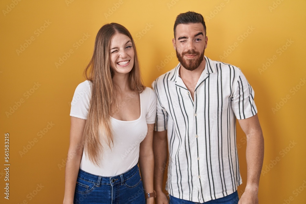 Young couple standing over yellow background winking looking at the camera with sexy expression, cheerful and happy face. Young couple standing over yellow background winking looking at the camera with sexy expression, cheerful and happy face.