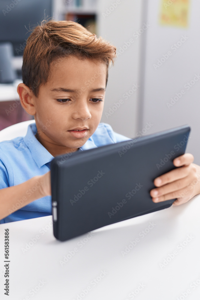 Adorable hispanic boy student using touchpad studying at classroom Adorable hispanic boy student using touchpad studying at classroom