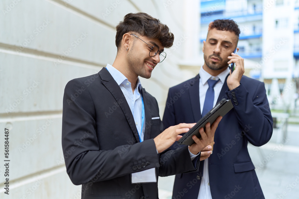Two hispanic men business workers using touchpad talking on smartphone at street Two hispanic men business workers using touchpad talking on smartphone at street