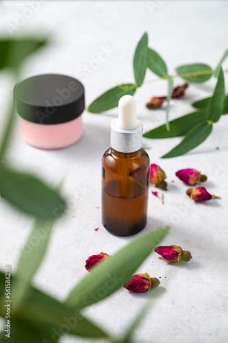 Face or body cream and serum in bottle with rose and eucalyptus on a light background close up. The concept of care cosmetics with herb.