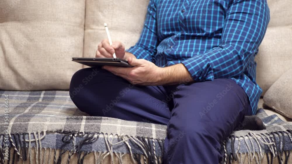 a man draws in an electronic tablet, sitting at home on a sofa. 4k. a man draws in an electronic tablet, sitting at home on a sofa. 4k.