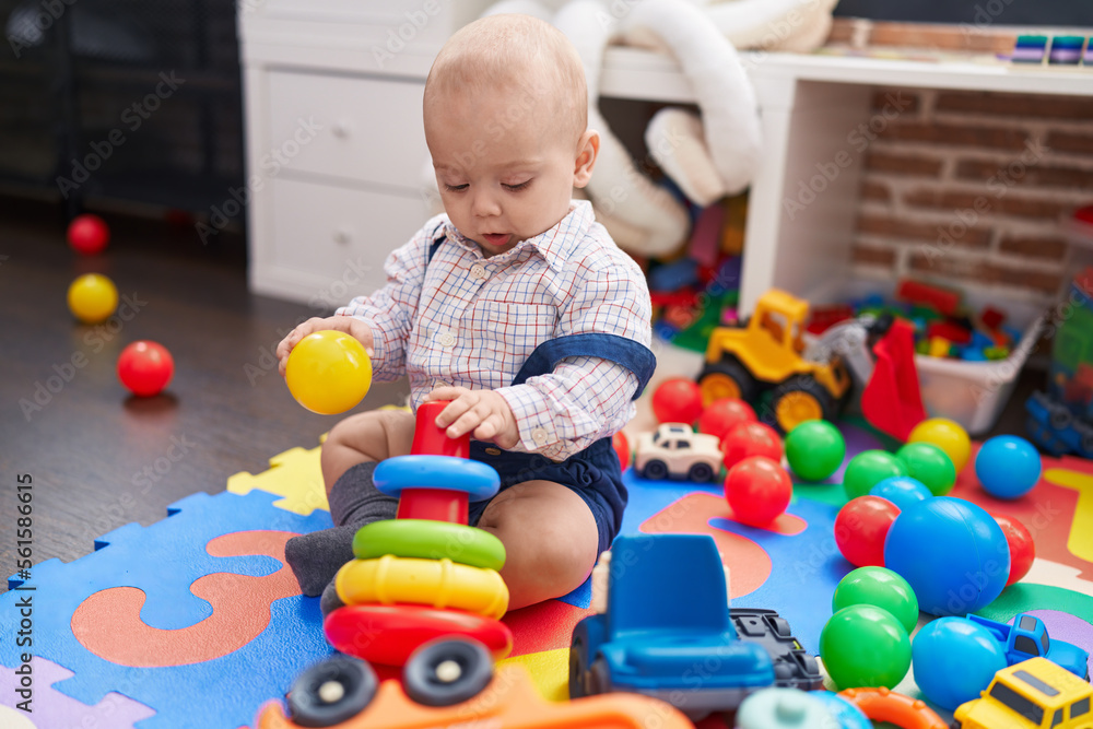 Adorable caucasian baby playing with balls and hoops sitting on floor at kindergarten Adorable caucasian baby playing with balls and hoops sitting on floor at kindergarten