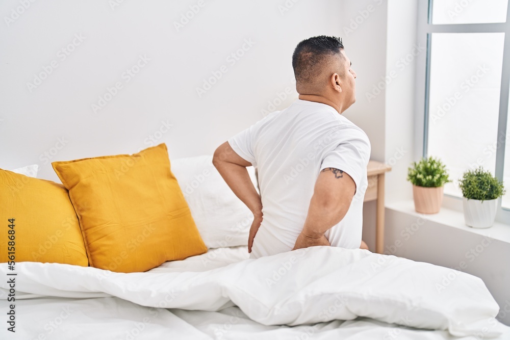 Young latin man suffering for back injury sitting on bed at bedroom Young latin man suffering for back injury sitting on bed at bedroom