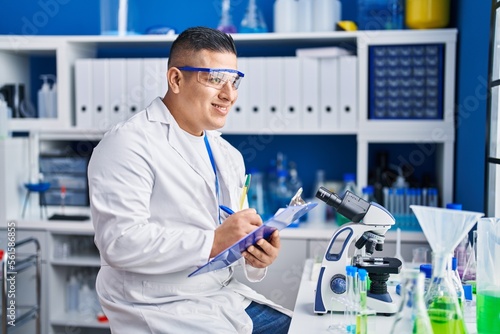 Young latin man scientist writing report working at laboratory