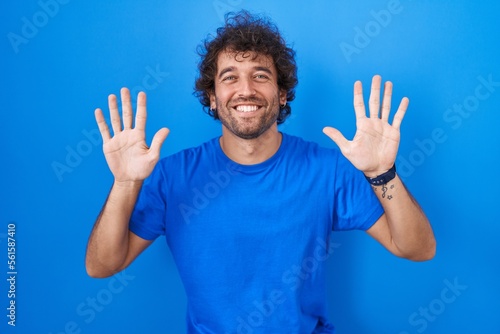 Hispanic young man standing over blue background showing and pointing up with fingers number ten while smiling confident and happy.