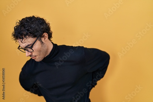 Hispanic man standing over yellow background suffering of backache, touching back with hand, muscular pain © Krakenimages.com