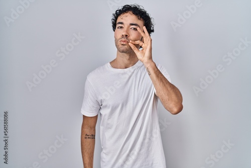 Hispanic man standing over isolated background mouth and lips shut as zip with fingers. secret and silent, taboo talking