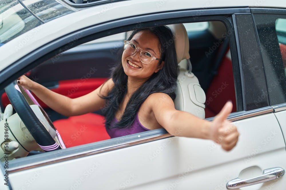 Young chinese woman driving car doing ok gesture with thumb up at street