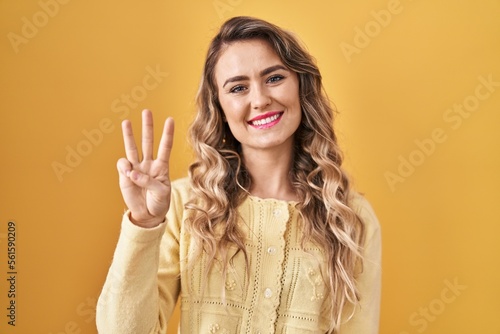 Young caucasian woman standing over yellow background showing and pointing up with fingers number three while smiling confident and happy.