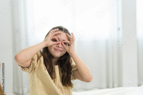 Happy child girl playing with her hands covering eyes in the living room at home