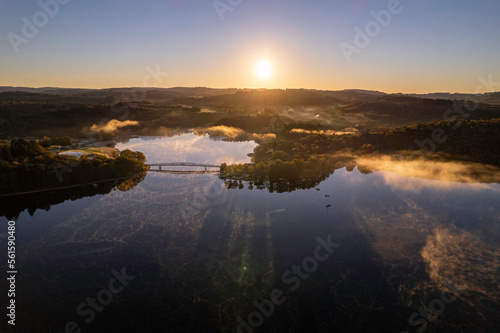 Aerial view of Lac de Saint Pardoux and its footbridge at sunrise in autumn with fog and mirror water
