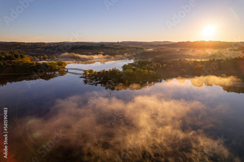 Aerial view of Lac de Saint Pardoux and its footbridge at sunrise in autumn with fog and mirror water