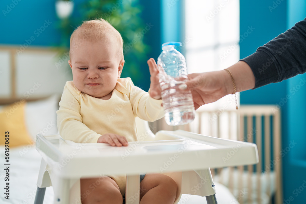 Adorable caucasian baby sitting on highchair rejecting bottle of water at bedroom Adorable caucasian baby sitting on highchair rejecting bottle of water at bedroom