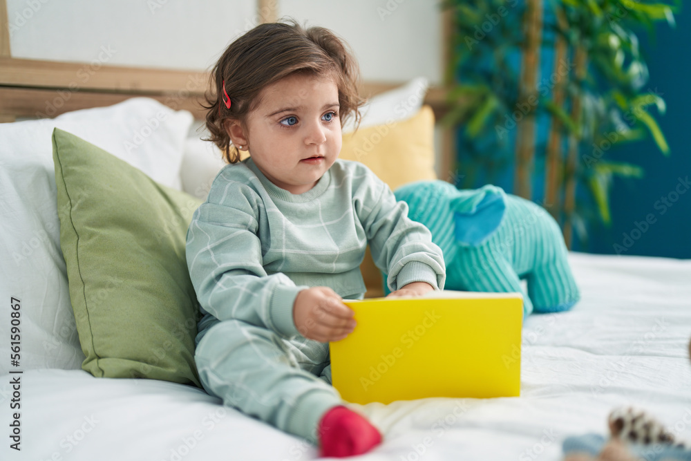 Adorable hispanic girl reading book sitting on bed at bedroom Adorable hispanic girl reading book sitting on bed at bedroom