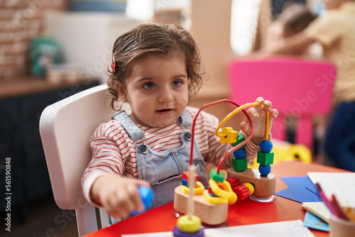 Adorable hispanic girl playing with toys sitting on table at kindergarten