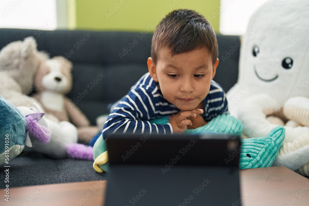 Adorable hispanic toddler watching video on touchpad sitting on sofa at home Adorable hispanic toddler watching video on touchpad sitting on sofa at home