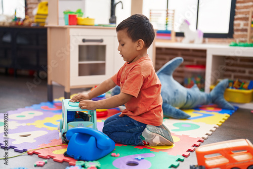 Adorable hispanic toddler sitting on floor with serious expression playing at kindergarten