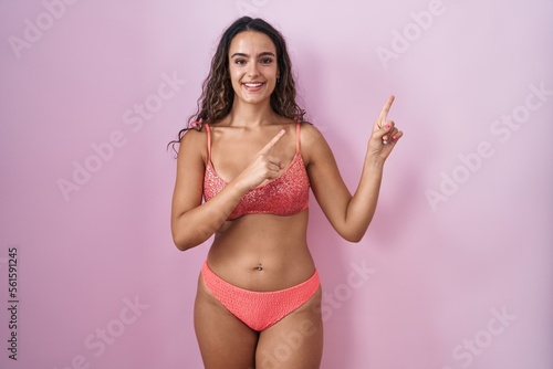 Young hispanic woman wearing lingerie over pink background smiling and looking at the camera pointing with two hands and fingers to the side.