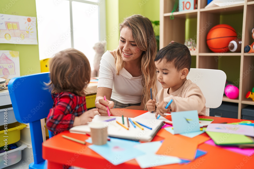 Teacher with boys sitting on table drawing on paper at kindergarten Teacher with boys sitting on table drawing on paper at kindergarten